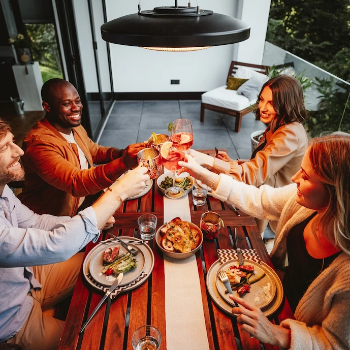 Freunde auf einem Balkon gemeinsam an einem Tisch darüber eine Heizstrahler