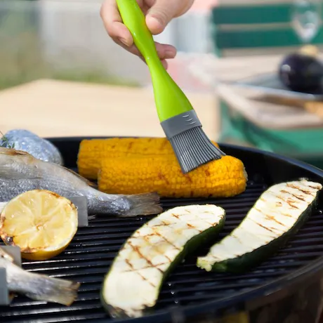 Person bestreicht Mais mit dem Silikonpinsel von Outdoorchef in Grün.