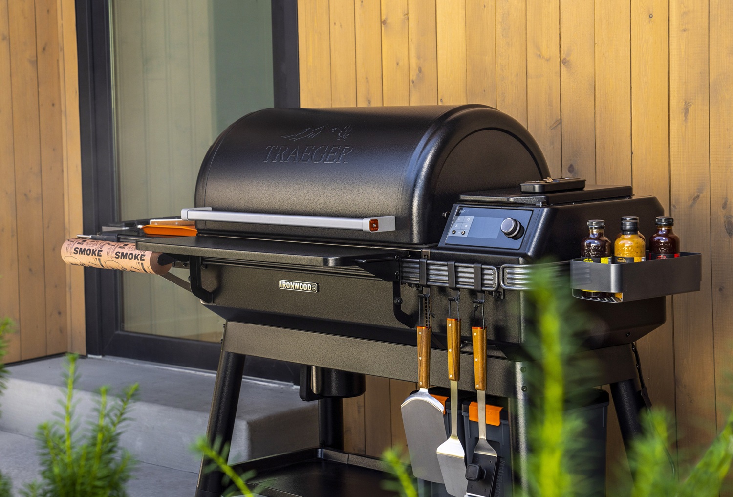 Smoker Traeger Ironwood XL mit Grillbesteck vor einer hölzernen Hauswand