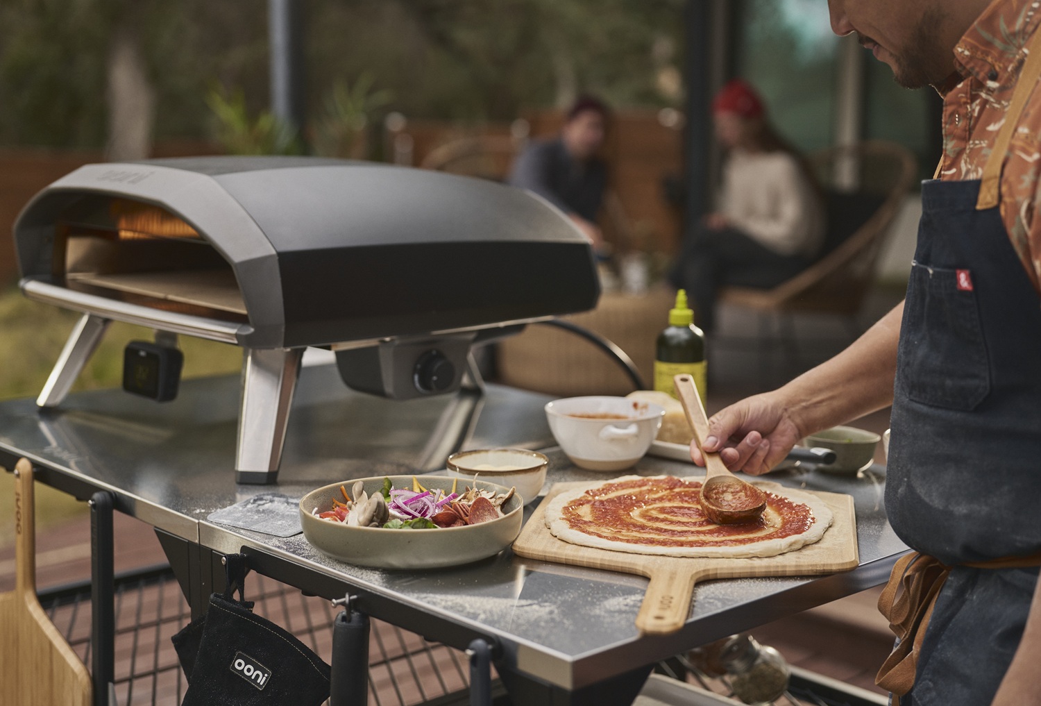 Ooni Koda 2 Pro Gas-Pizzaofen auf einem Tisch, daneben bereitet ein Mann die nächste Pizza vor