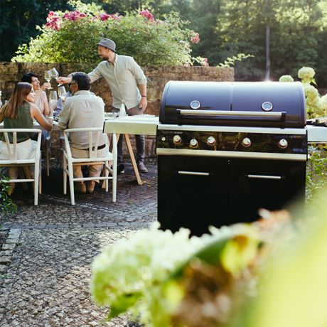 Gruppe von Menschen speist im Freien neben einem Gasgrill