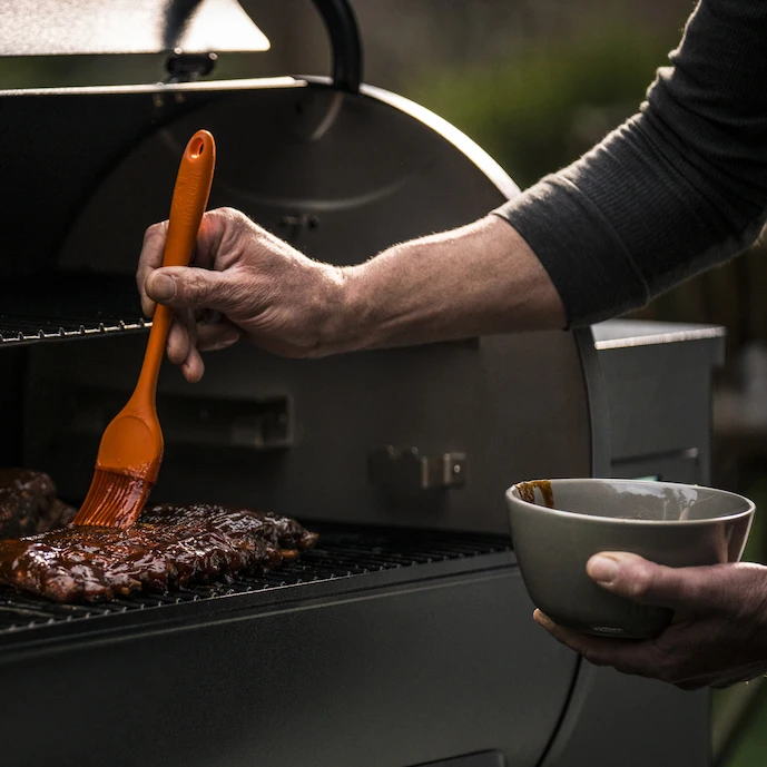 Fleisch wird mit einer Sauce mit einem Siliconpinsel eingestrichen