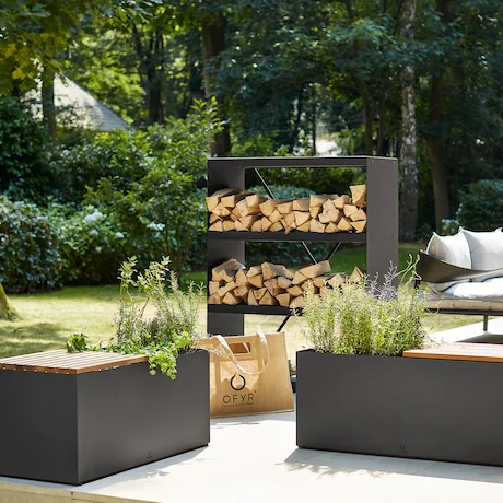 Ein Garten mit moderner Einrichtung, darunter ein Holzlagerregal, eine Bank mit Pflanzenkästen und eine bequeme Sitzgelegenheit.
