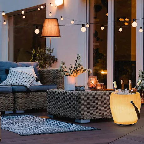 Gemütliche Terrasse mit Sofas, Kissen, einer beleuchteten Eiskühlbox und dekorativen Lichtern Gemütliche Terrasse mit Sofas, Kissen, einer beleuchteten Eiskühlbox und dekorativen Lichtern