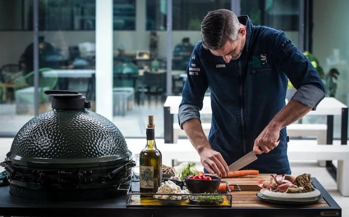 Big Green Egg Keramikgrill im Einsatz daneben ein Mann bei der Zubereitung und Vorbereitung des Grillguts