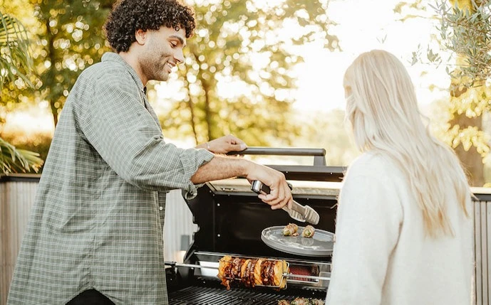 Mann und Frau an einem Gasgrill mit Drehspieß