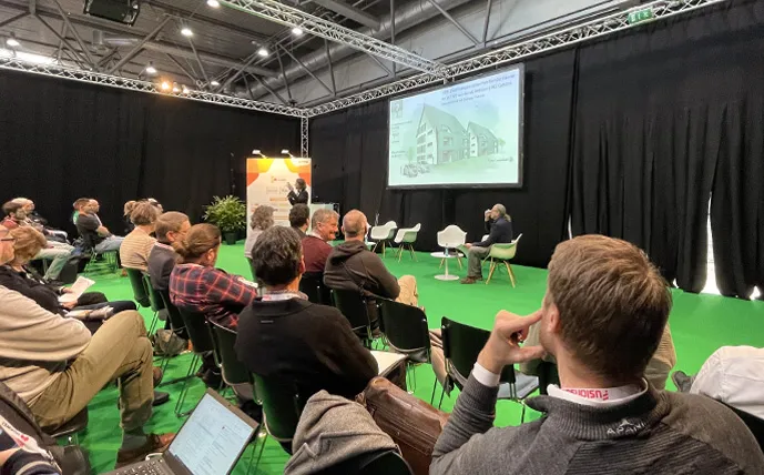 Viele Personen sitzen und hören einem Vortrag in der Messehalle zu