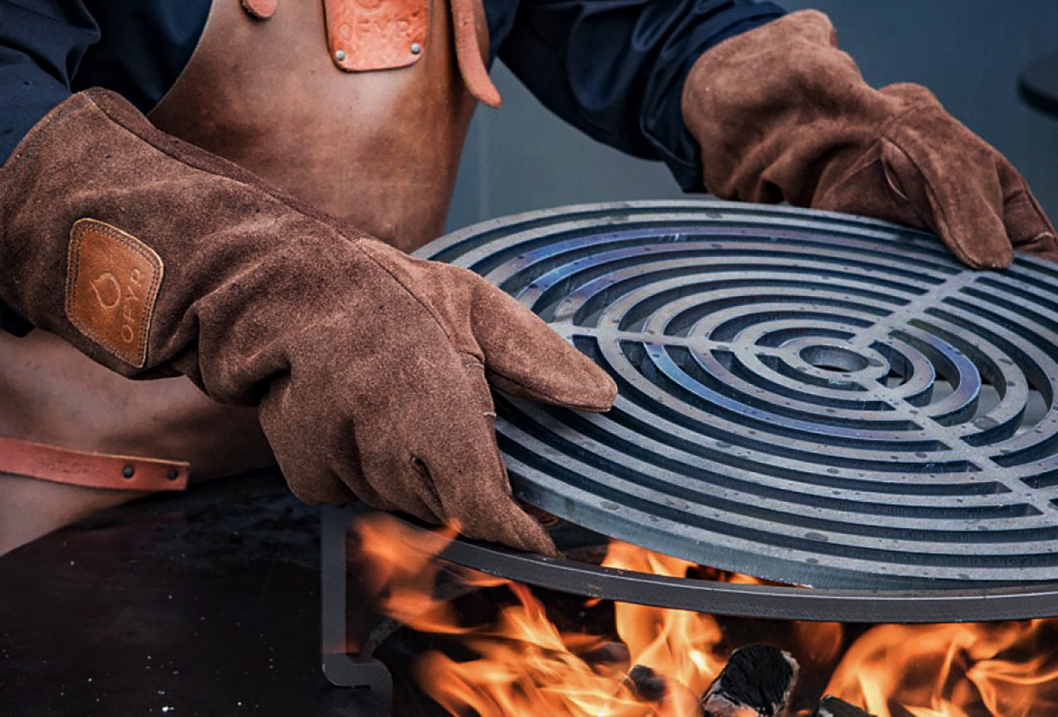 OFYR Grillhandschuhe setzen einen Grillrost über dem Feuer ein